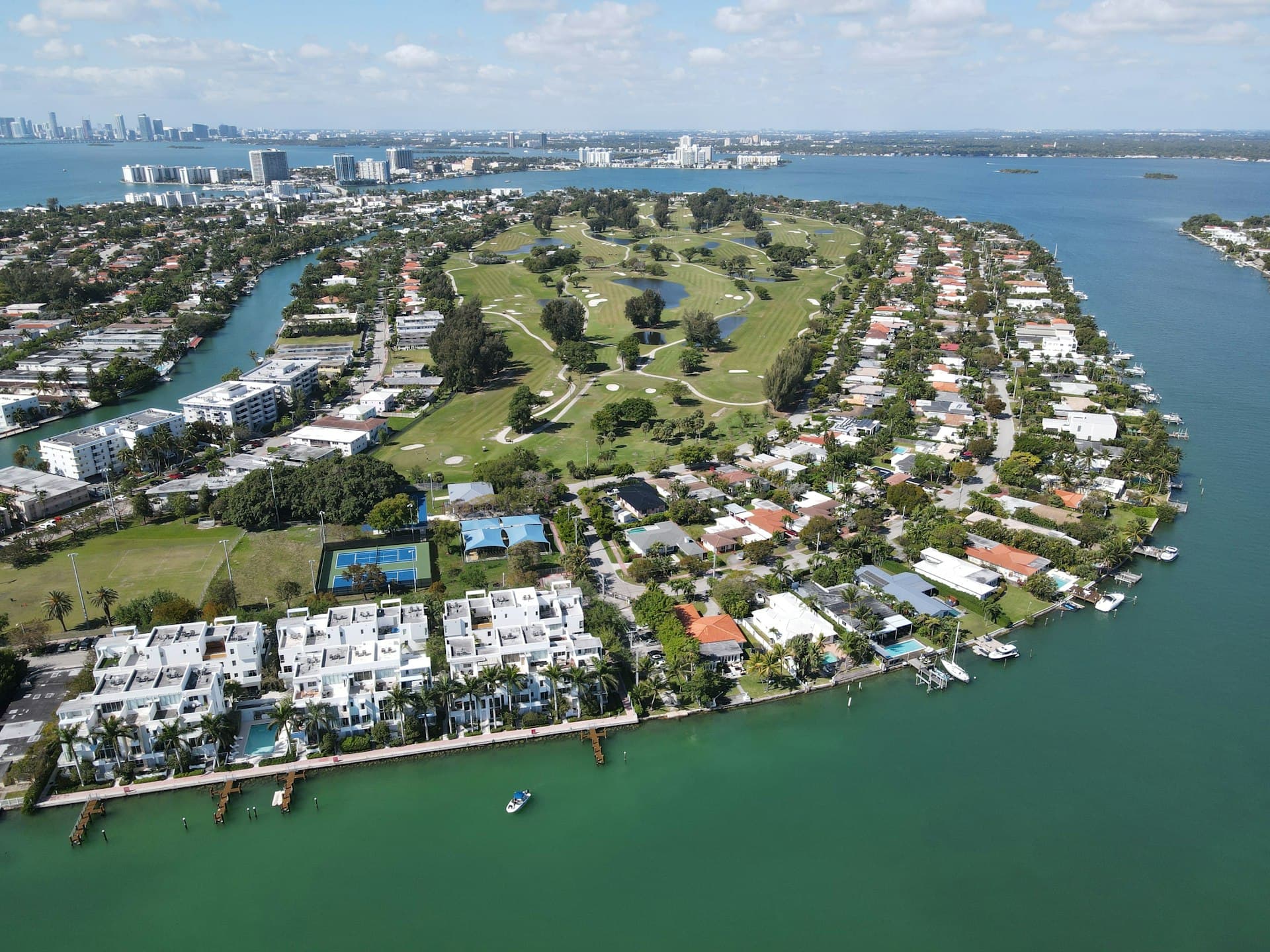Aerial view of Miami Beach golf course community with waterfront homes and boats